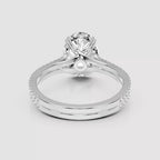 A silver-toned diamond engagement ring with a round-cut center stone, crossed band details, and a pavé band, shown on a light gray background.