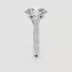 A high-end diamond solitaire engagement ring with a brilliant round-cut center stone and a pavé-set diamond band in a silver-colored metal, shown against a neutral light gray background.