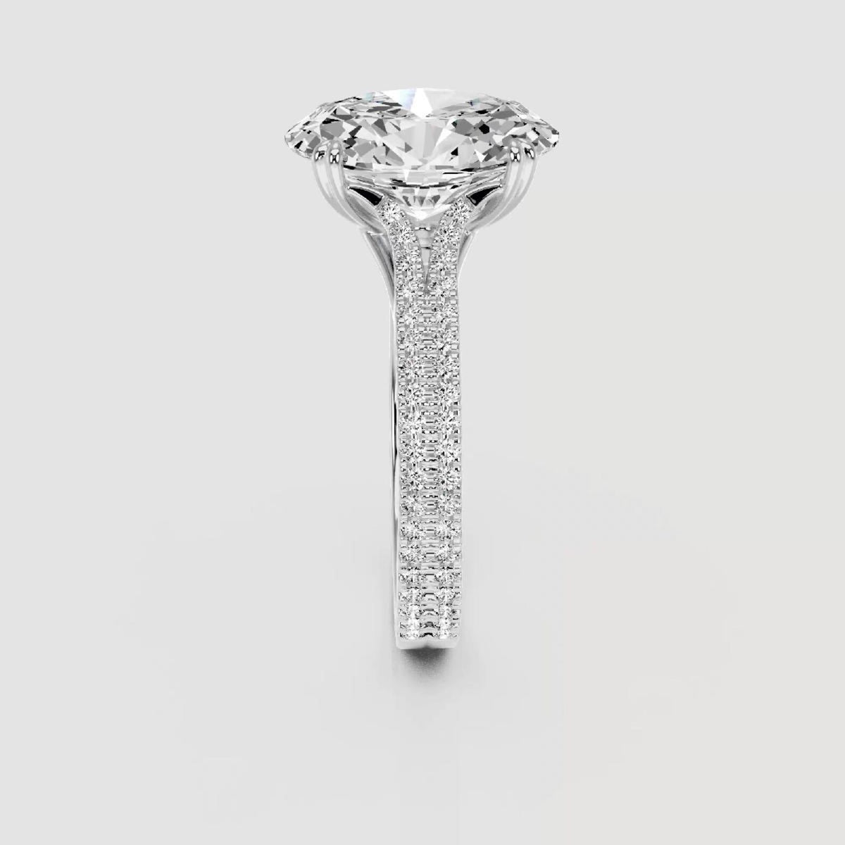 A high-end diamond solitaire engagement ring with a brilliant round-cut center stone and a pavé-set diamond band in a silver-colored metal, shown against a neutral light gray background.