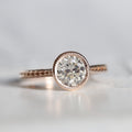 Front view of a 2 CT round lab grown diamond engagement ring in a rose gold milgrain bezel setting with a braided textured band.