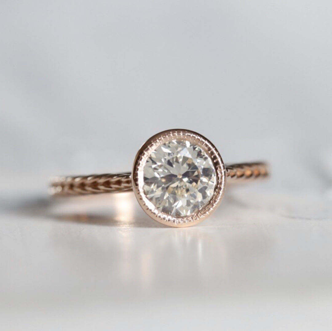 Front view of a 2 CT round lab grown diamond engagement ring in a rose gold milgrain bezel setting with a braided textured band.