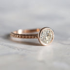 Angled close-up of a 2 CT round brilliant lab-created diamond set in a rose gold bezel ring with milgrain detailing