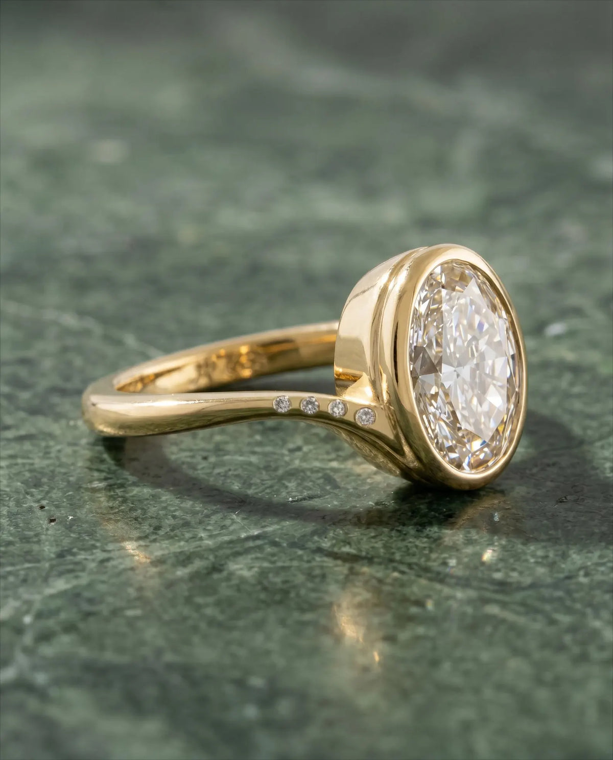 Three-quarter side angle showing full bezel profile and flush-set accent diamonds along the curved yellow gold shoulder of 3 Carat Oval Ring