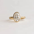 Top-down view of 2 Carat Oval Cut Lab Grown Diamond Bezel Ring in yellow gold with celestial star-set accent diamonds