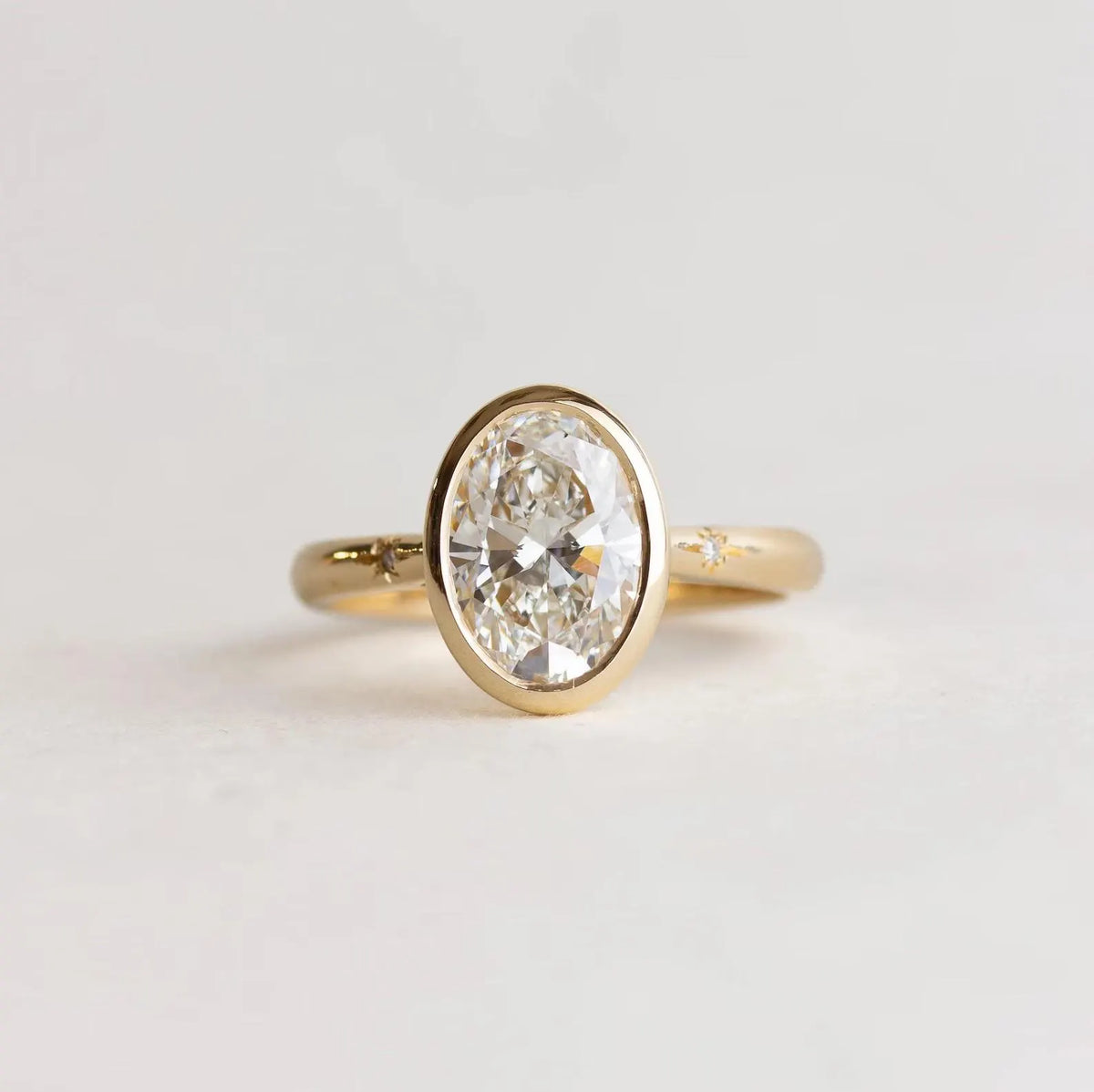 Top-down view of 2 Carat Oval Cut Lab Grown Diamond Bezel Ring in yellow gold with celestial star-set accent diamonds
