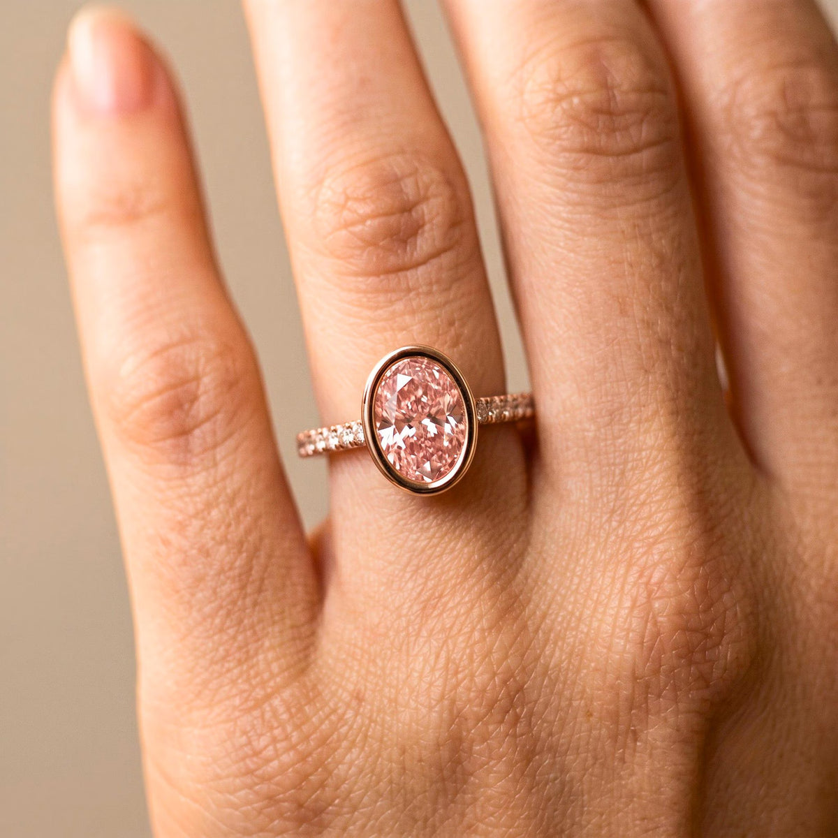 On-hand view of 2 Carat Pink Oval Cut Lab Grown Diamond Bezel Engagement Ring with pave diamond band in rose gold