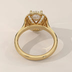 A yellow gold ring with a triangular clear gemstone center and a halo of small round diamonds, shown from a top-down angle on a light beige background.