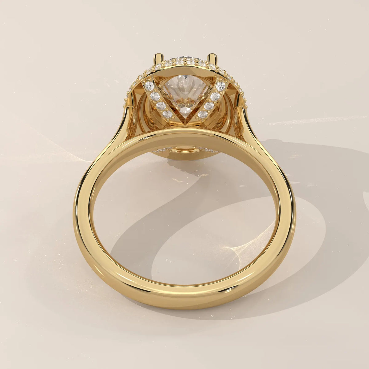 A yellow gold ring with a triangular clear gemstone center and a halo of small round diamonds, shown from a top-down angle on a light beige background.
