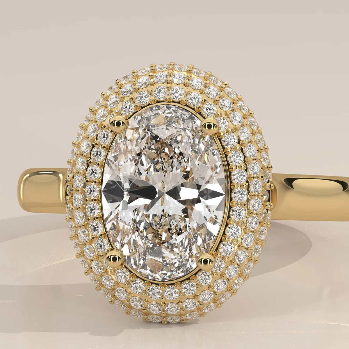 An oval halo ring featuring a large oval-cut center stone surrounded by double rows of small pavé-set diamonds, set in yellow gold on a matching band, shown against a neutral light beige background.
