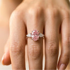 A close-up of a hand wearing a silver ring with a large oval pink gemstone and smaller side stones.