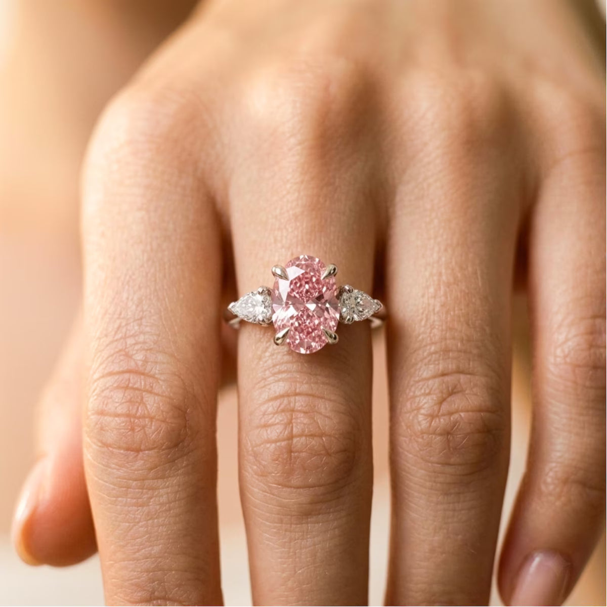 A close-up of a hand wearing a silver ring with a large oval pink gemstone and smaller side stones.