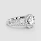 A silver-toned diamond ring with a round-cut center stone surrounded by a halo and pavé-set side stones on a light gray background.