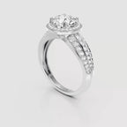 A silver-toned diamond ring with a round-cut center stone, a halo of smaller diamonds, and a split shank paved with diamonds, shown on a light gray background.