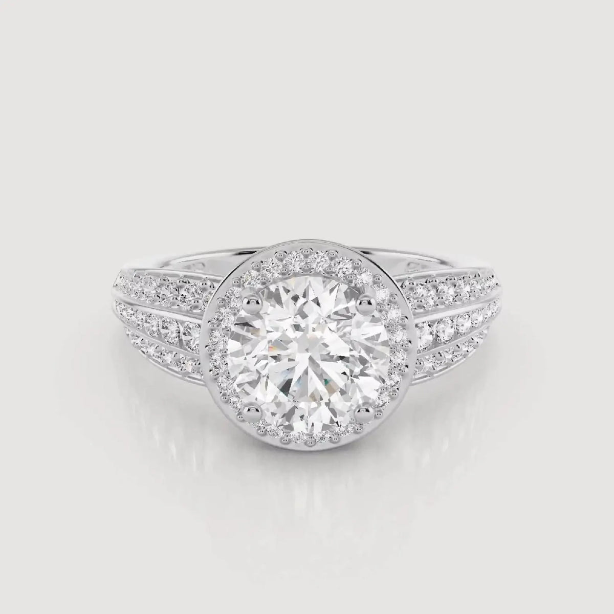 A silver-toned diamond ring with a large round center stone surrounded by a halo, and smaller diamonds set along the split shank, shown on a light gray background.