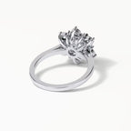 A silver-toned ring with a large, intricate floral or starburst cluster setting, photographed on a clean white background with a soft shadow.