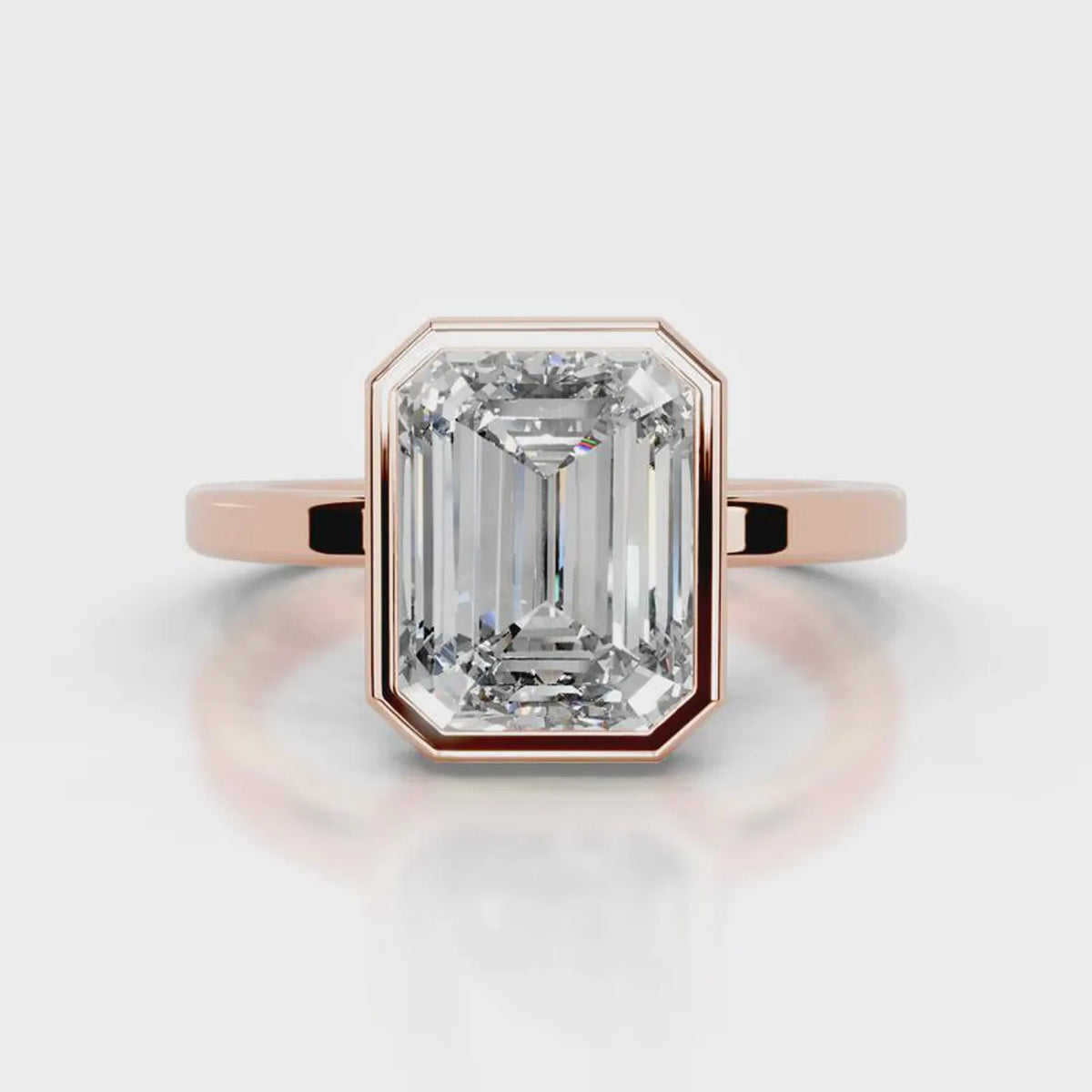 An emerald-cut diamond ring set in rose gold, featuring a prominent rectangular gemstone in an octagonal bezel setting on a polished band, shown against a light gray background with a soft reflection.