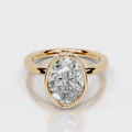 A yellow gold ring featuring a large, oval-cut clear gemstone in a bezel setting, shown on a clean light gray reflective surface.