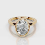 A yellow gold ring featuring a large, oval-cut clear gemstone in a bezel setting, shown on a clean light gray reflective surface.