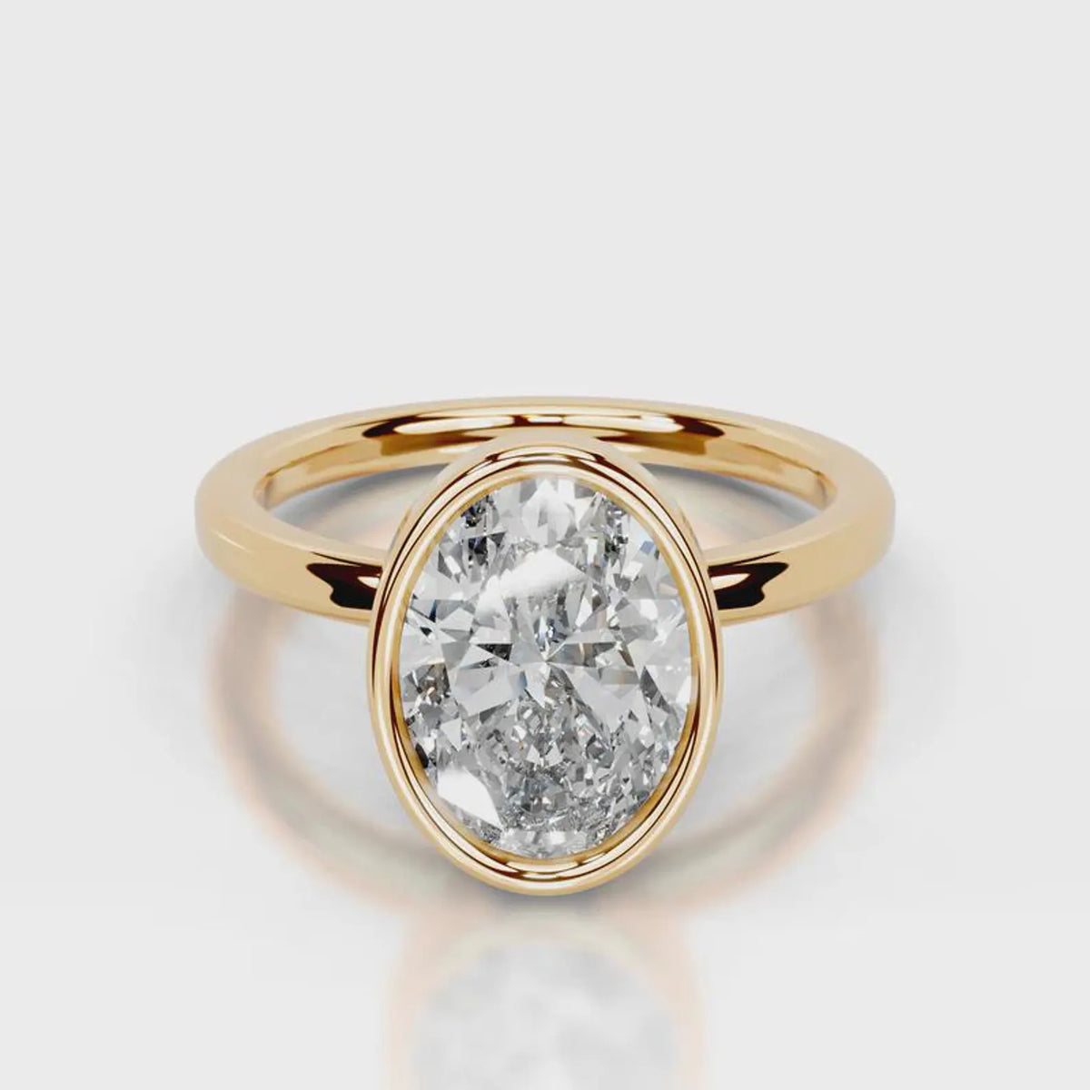 A yellow gold ring featuring a large, oval-cut clear gemstone in a bezel setting, shown on a clean light gray reflective surface.