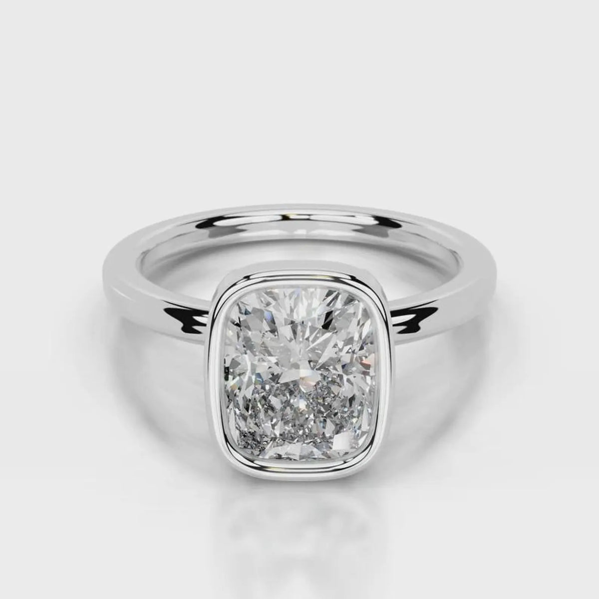 A radiant cut diamond engagement ring in a polished silver-colored metal band, shown on a clean light gray background with a soft reflection.