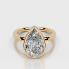 A pear-cut diamond ring in a yellow gold setting with a split shank band, shown on a light gray reflective surface.