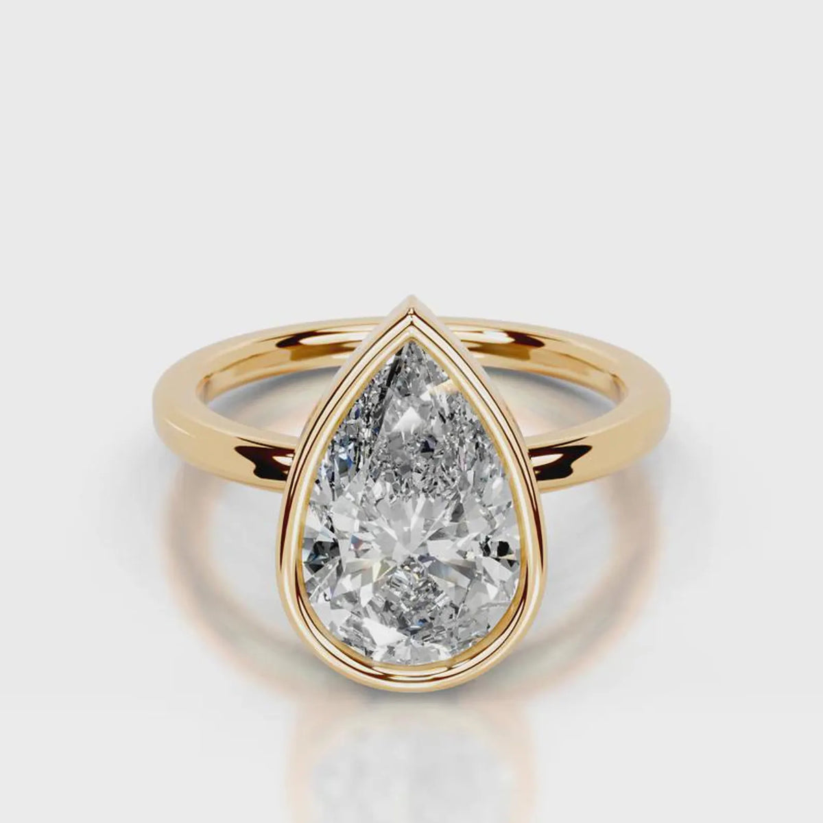 A pear-cut diamond ring in a yellow gold setting with a split shank band, shown on a light gray reflective surface.