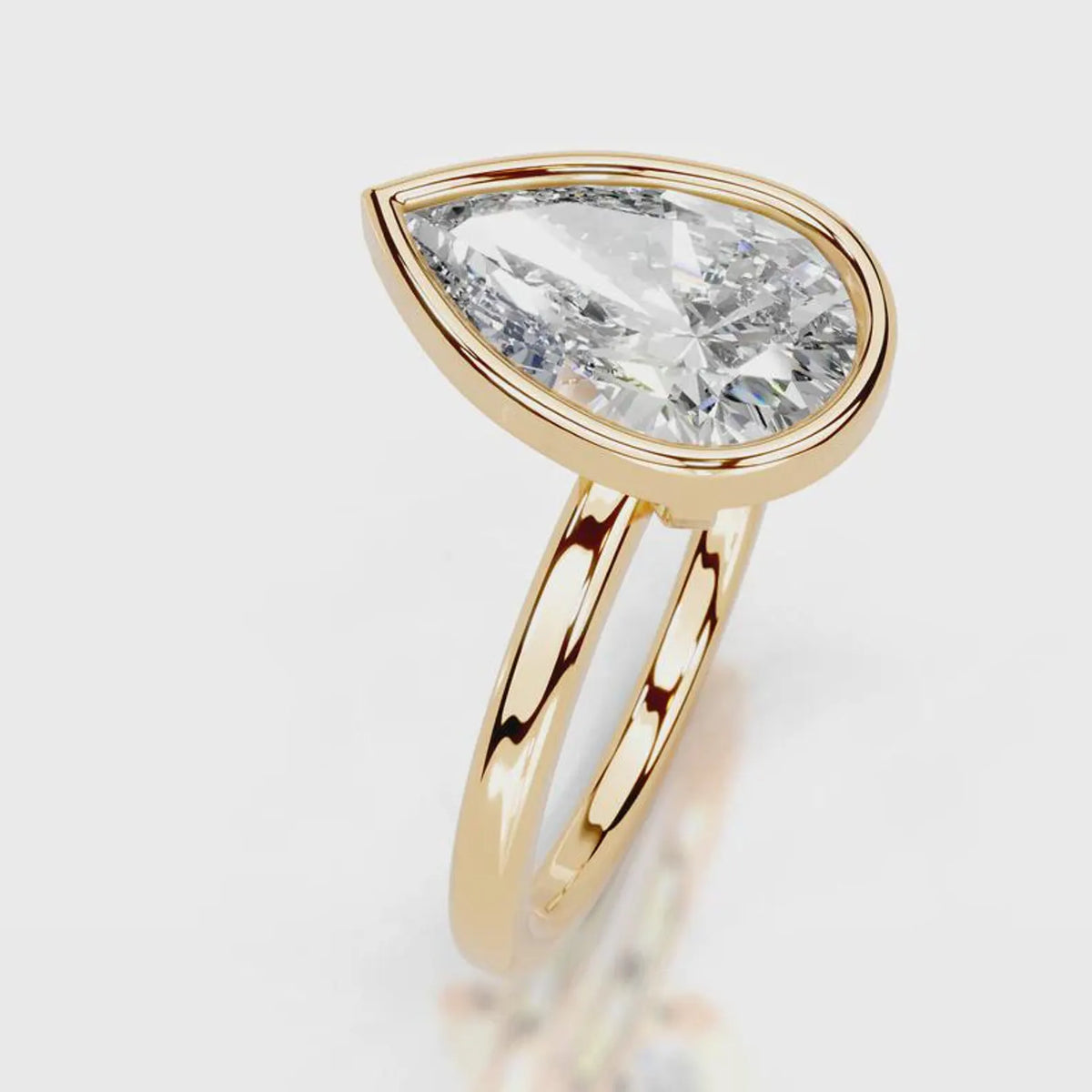A gold ring featuring a large teardrop-shaped clear gemstone in a bezel setting, with a polished double-band design, shown on a light gray background.