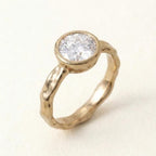 3 carat round lab grown diamond bezel engagement ring with a yellow gold organic hammered band displayed at a three-quarter angle.