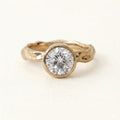 Top-down front view of a sparkling 3 carat round brilliant lab grown diamond in a smooth gold bezel with textured band.