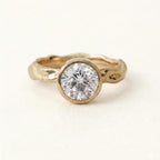 Top-down front view of a sparkling 3 carat round brilliant lab grown diamond in a smooth gold bezel with textured band.