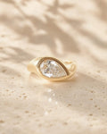 Front top-angle view of a 2 carat pear cut lab grown diamond set in a chunky yellow gold bezel ring.