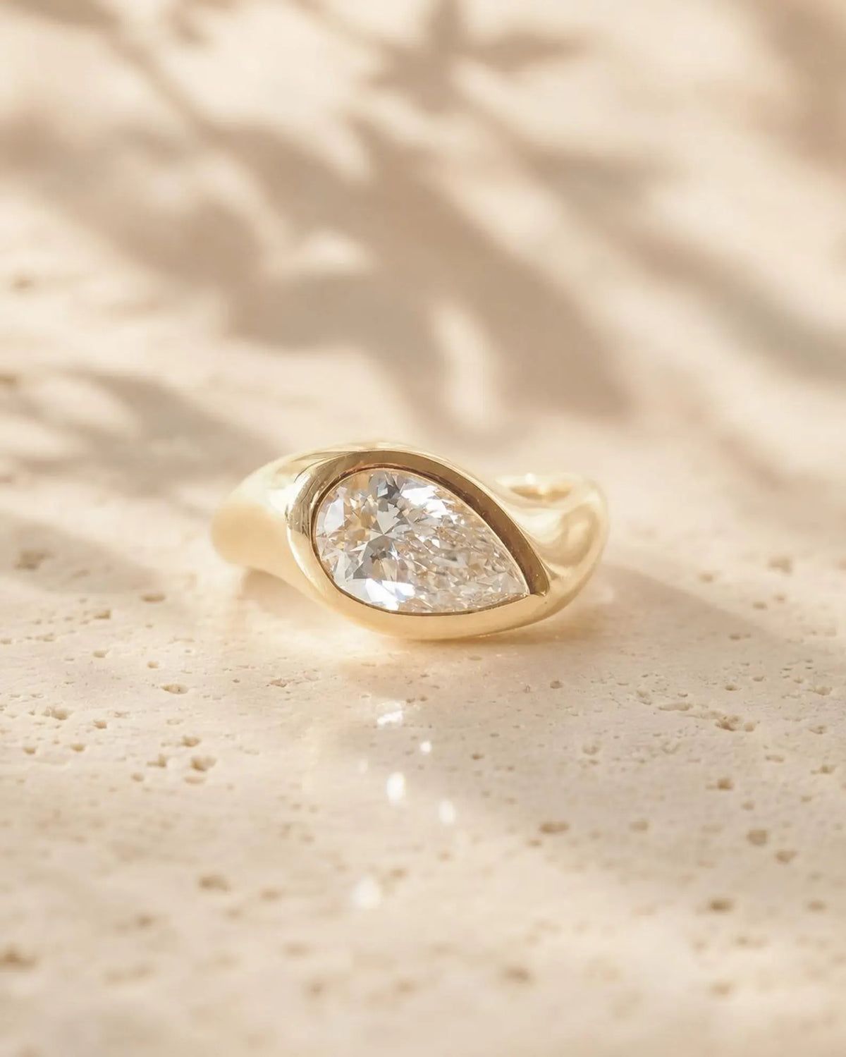 Front top-angle view of a 2 carat pear cut lab grown diamond set in a chunky yellow gold bezel ring.