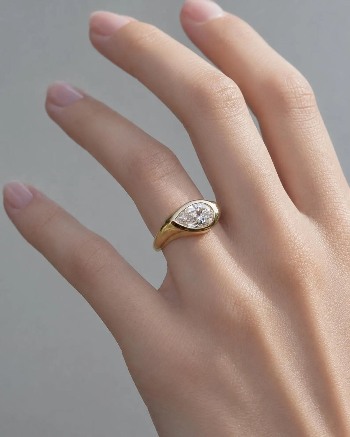 On-hand view of a modern 2 carat pear cut lab grown diamond chunky bezel signet ring on a woman's finger.