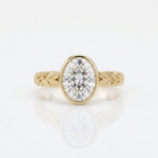 Front top view of a 3 carat oval cut lab grown diamond bezel set ring in yellow gold with leaf engraved band.