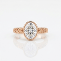Front view of a 3 carat oval lab grown diamond bezel engagement ring in rose gold with botanical leaf engraving.