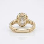 Underside back view of a yellow gold 3 ct oval lab diamond ring with leaf-engraved bezel basket structure.