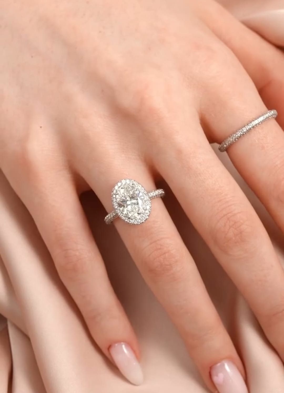 Full hand modeling shot of a 3 CT oval lab diamond halo engagement ring paired with a pavé stackable band.