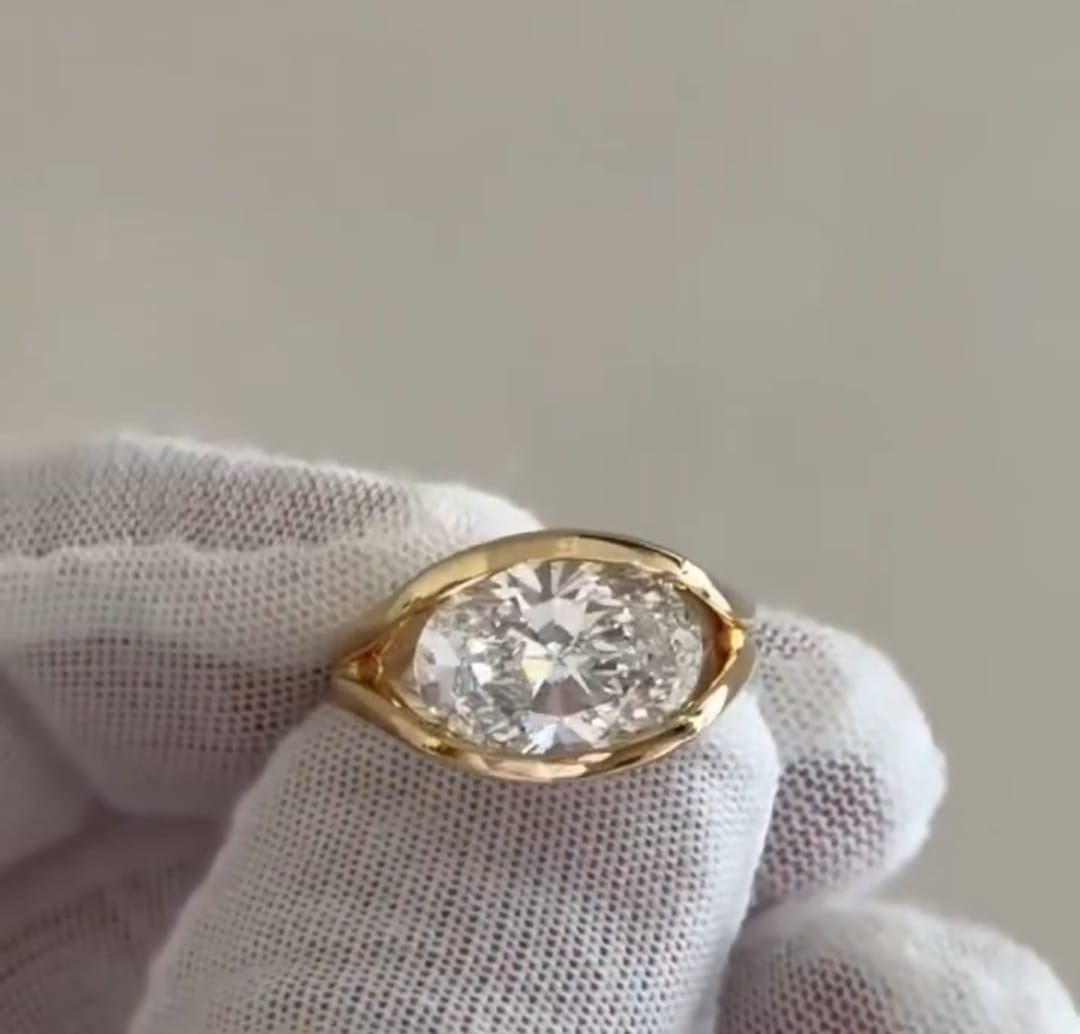 Top-down view of a 4 carat oval cut lab grown diamond set horizontally in a yellow gold bezel frame.