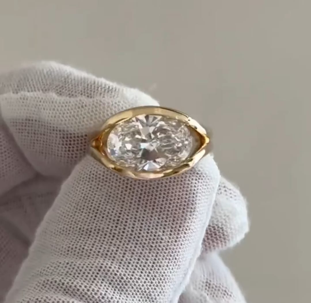 Direct top view of a modern 4 ct East-West oval lab diamond bezel engagement ring in yellow gold.