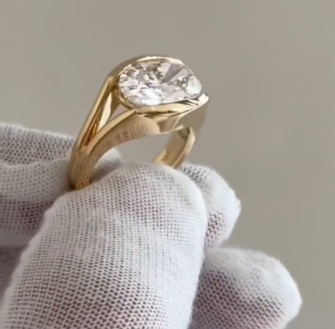 Perspective side view showing the thick 18K yellow gold band and low profile bezel setting of a 4 ct oval lab diamond ring.