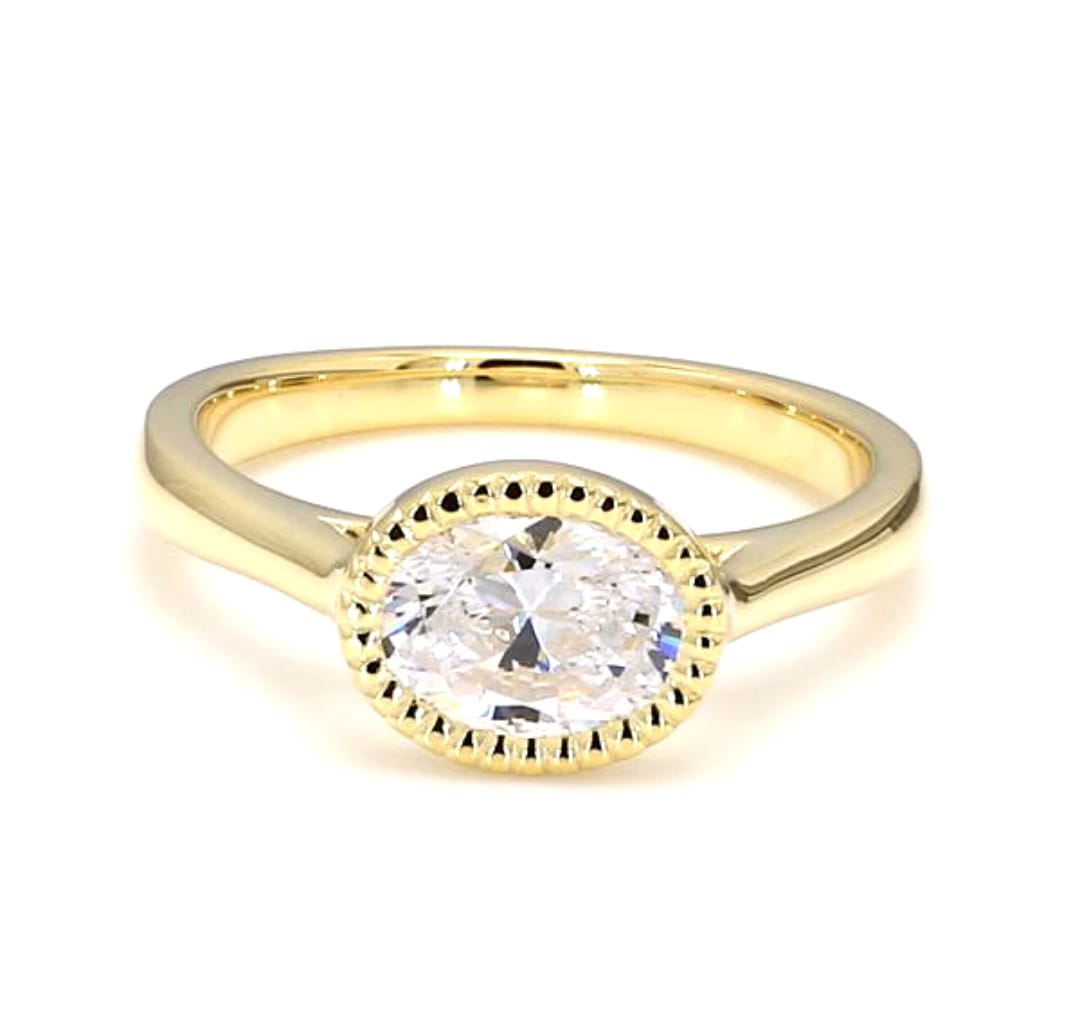 Top-down view of a 2 CT oval cut lab grown diamond set horizontally in a yellow gold milgrain bezel ring.