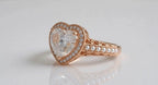 Three-quarter perspective of rose gold heart diamond ring on white reflective surface.