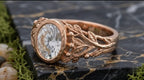 Low angle view highlighting sculpted vine branch band and bezel set oval center stone.