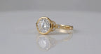 Angled studio shot of yellow gold bezel round diamond ring with leaf shoulders and twisted vine band.