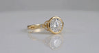 Side-angled studio shot highlighting leaf shoulders and bezel set round diamond center.