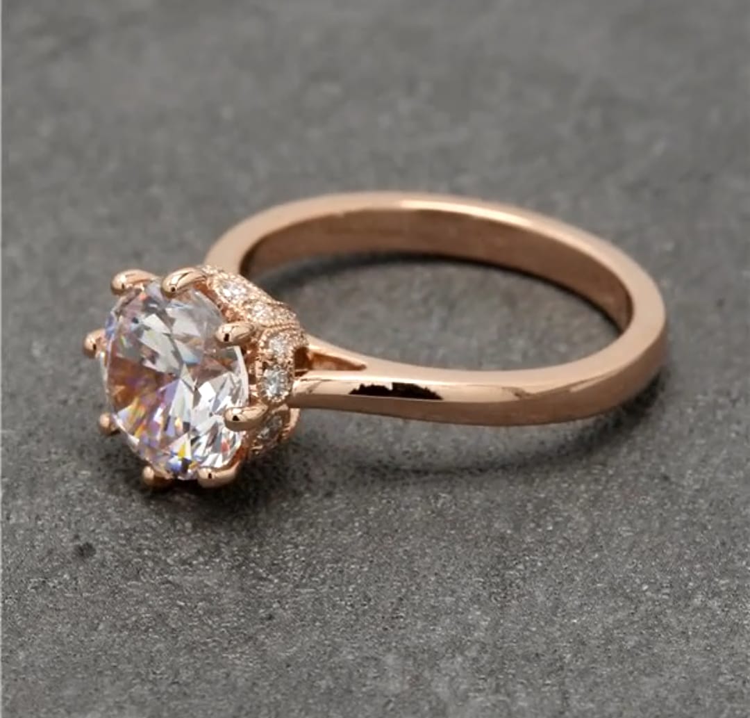 Three-quarter angle view of a 2 CT round lab grown diamond engagement ring with a rose gold band and ornate crown gallery.