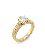 Perspective view of a 3 CT round cut lab diamond solitaire ring featuring relief scrollwork engraving on a 14K yellow gold band.