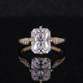 Top face-up view of a 2 CT radiant cut lab diamond ring featuring milgrain-detailed leaf shoulders on a reflective black background.
