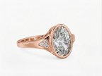 Three-quarter view of a rose gold 3 CT oval lab diamond engagement ring showing bezel setting and pave cluster shoulders.