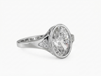 Angled view of a 3 CT oval cut lab grown diamond bezel engagement ring in white gold with pave shoulder accents.